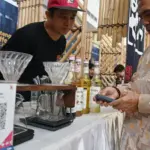 Warga menyiapkan gadgetnya untuk pembayaran melalui QRIS di salah satu outlet kopi di Palu, Sabtu (18/10/2025). (© bmzIMAGES/Basri Marzuki)
